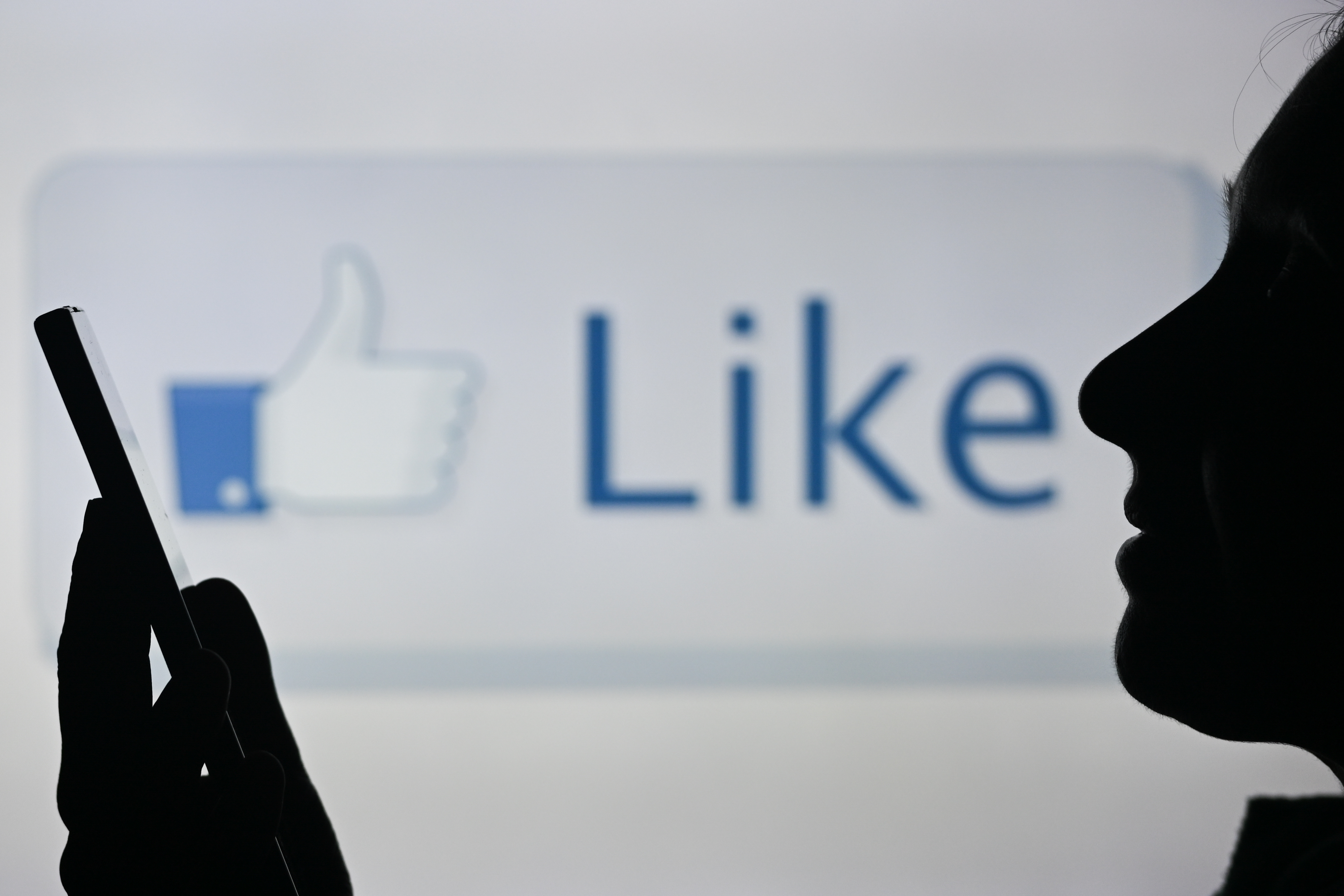 An image of a woman holding a cell phone in front of a LIKE symbol