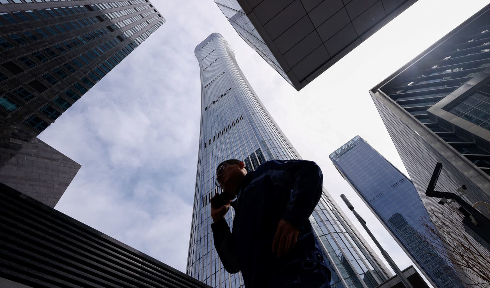 A man walks past buildings at Central Business District (CBD) in Beijing, China April 8, 2025. 